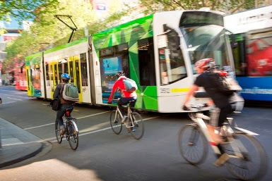 People riding bikes along the road, past a tram.