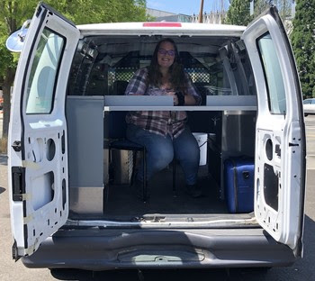 Photo of person sitting in back of van facing out the rear doors