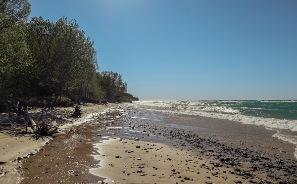 long view of the sandy, rocky beach, blue sky and shoreline waves at Muskellonge State Park in Luce County