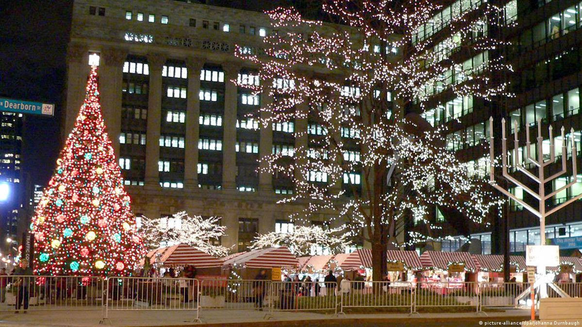 Árvore de Natal com luzes e barraquinhas em uma praça à noite.