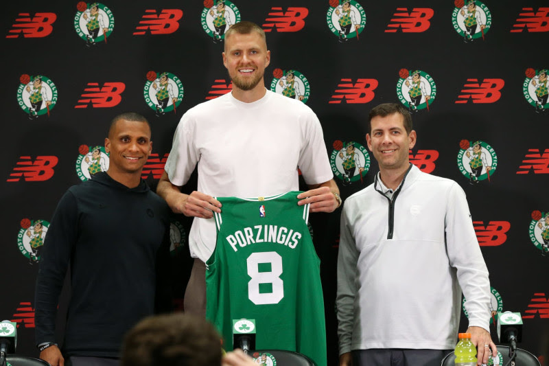 Boston, MA - June 29: Boston Celtics C Kristaps Porzingis holds up his number eight Celtics jersey at his introductory press conference, flanked by head coach Joe Mazzulla and President of Basketball Operations Brad Stevens. (Photo by Jonathan Wiggs/The Boston Globe via Getty Images)