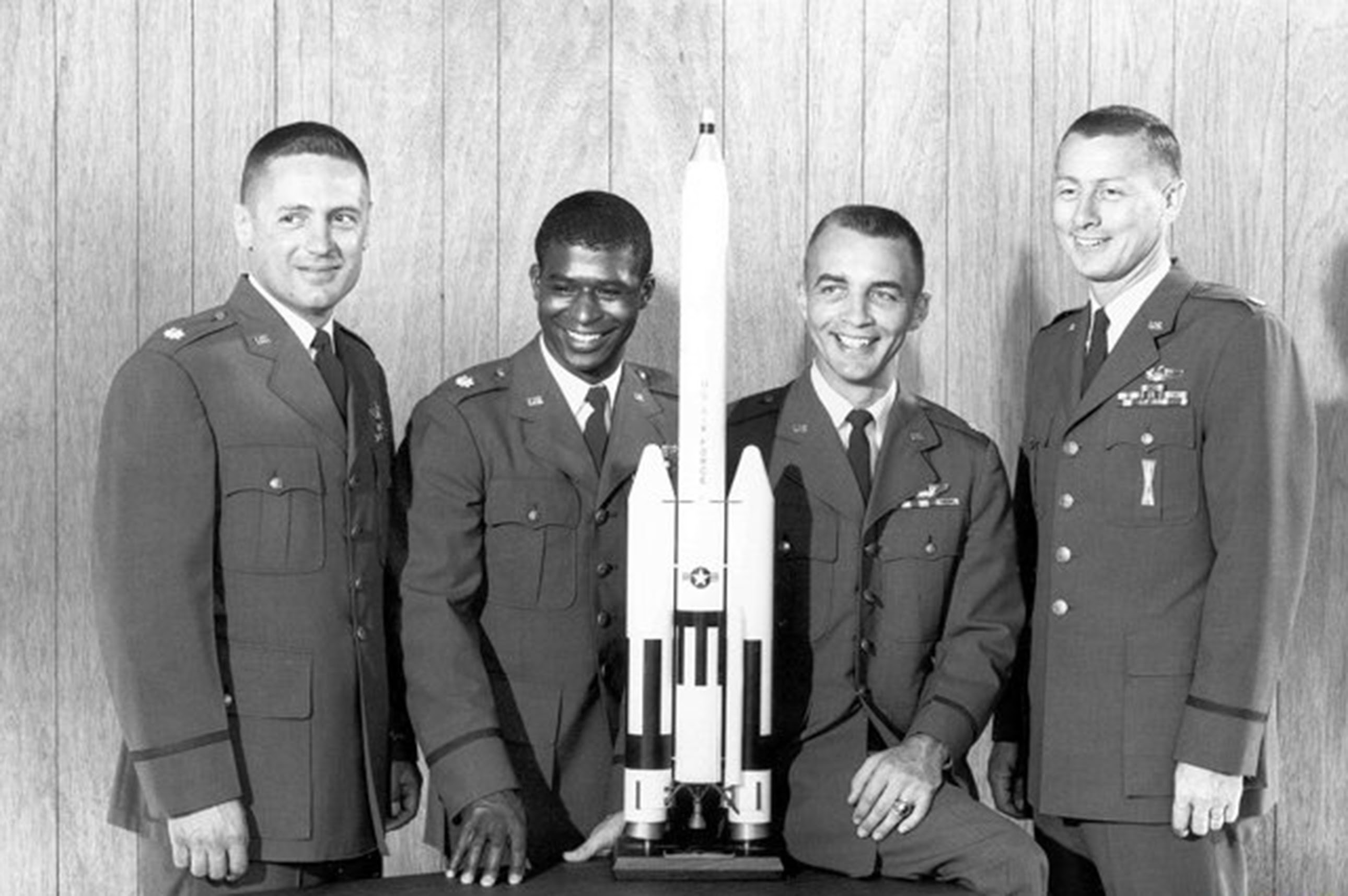 a group of uniformed men smiling and posing with a model rocket
