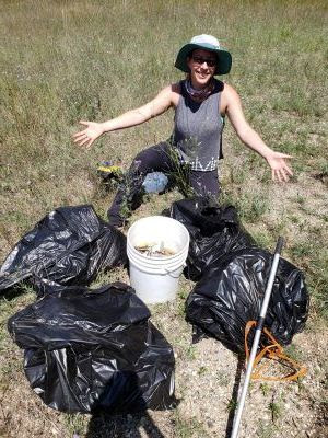 A person poses next to buckets and bags of trash cleaned from the forest