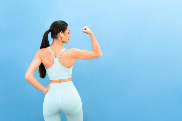 Young beautiful woman spends time in the home gym shows her muscles on a blue background training sport concept