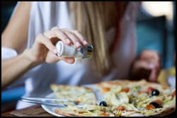 The figure above is a photograph of a woman putting extra salt on her pizza.