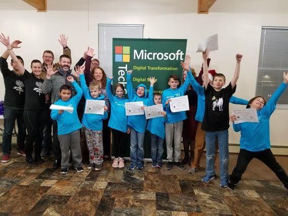 A mix of elementary and middle school students hold their Hour of Code completion certificates and raise their hands in excitement with State Superintendent Jillian Balow, and staff from Microsoft and the Array School of Technology and Design. They are all standing in from of a Microsoft banner.