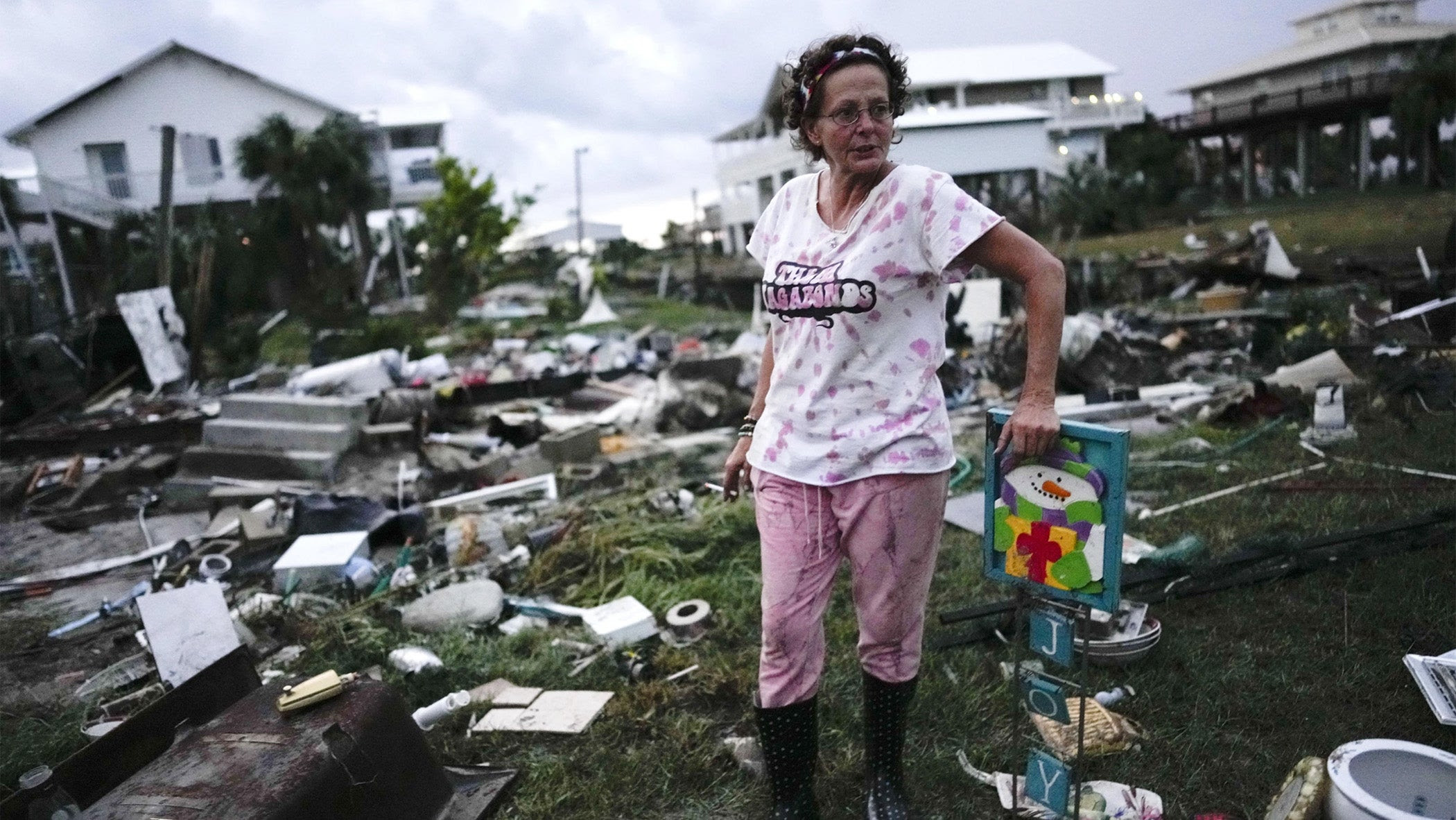 a woman stands in the wreckage, holding a Christmas decoration