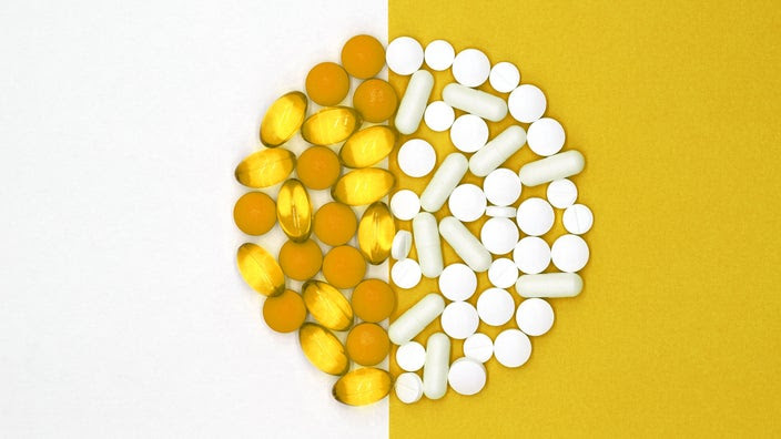 Various yellow and white pills in a pile to form two half circles on a yellow and white background.