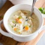Chicken and wild rice soup in a white soup bowl with a spoon, served on a wood board with another bowl of soup in the background.