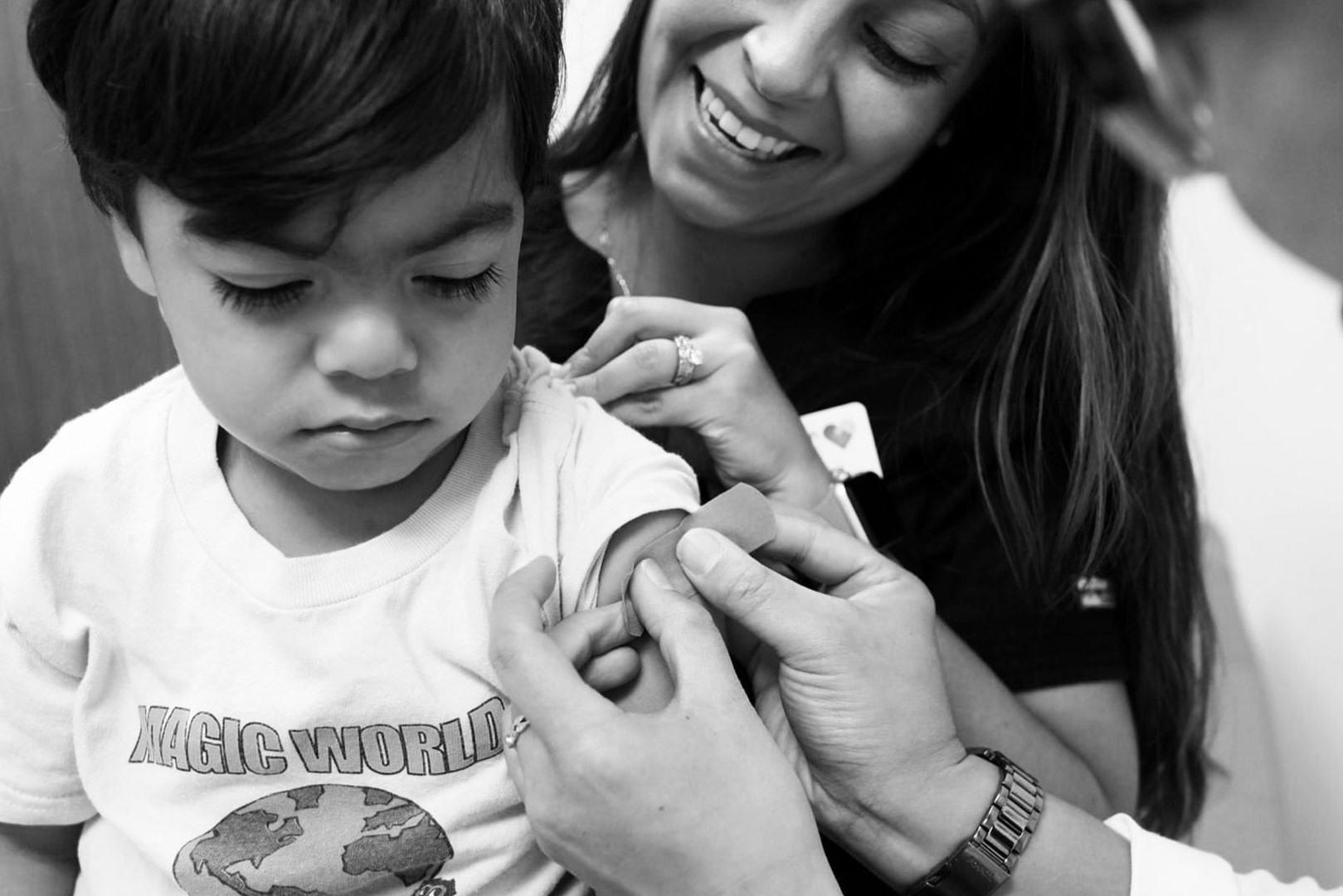 An image of an individual with a smile, holding a young person while they receive a vaccination jab.
