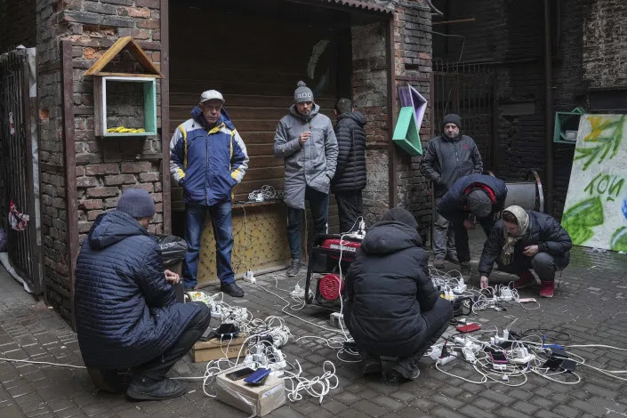 People stand and crouch as they charge their phones in a courtyard in Mariupol. 