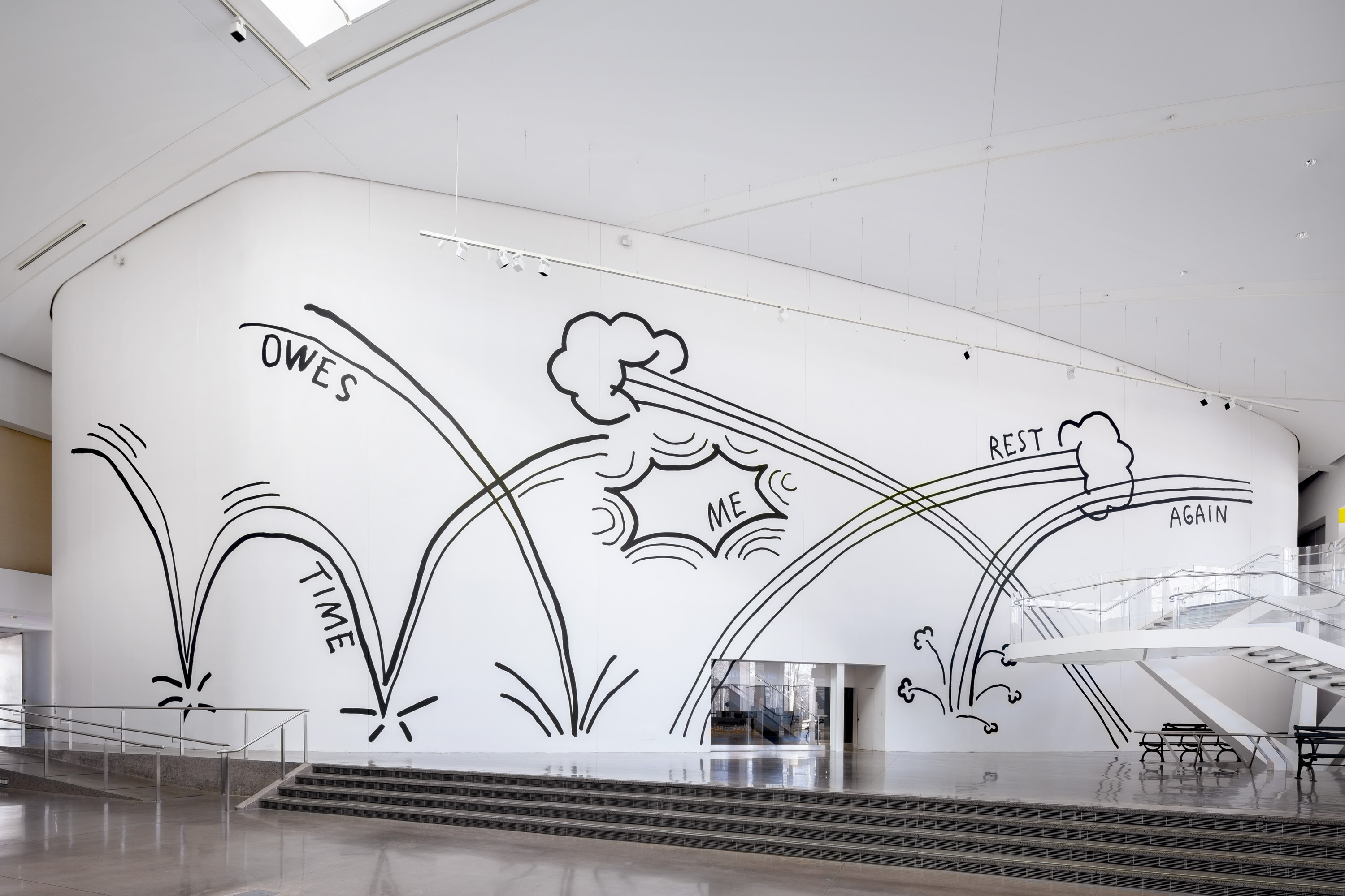 An installation shot of Christine Sun Kim's new mural "Time Owes Me Rest Again". Photo: Hai Zhang. The photo shows a monumental wall at the center of the Queens Museum with painted illustrations inspired by comic book graphics that are commonly used to represent movement and contact. Five words appear "Time", "Owes", "Me", "Rest", "Again". 