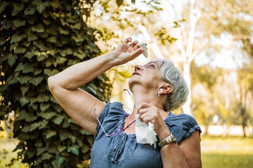 Older woman leaning back slightly to use eye drops while outside.