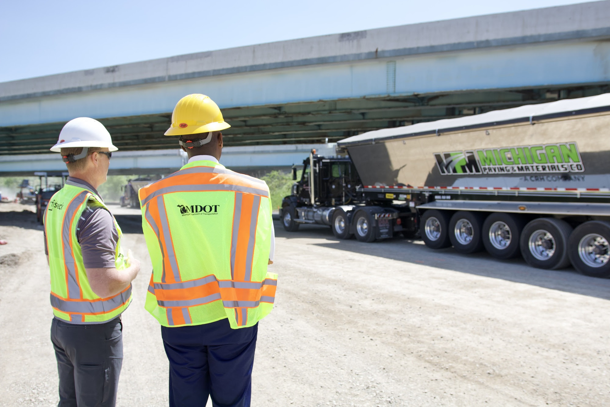 Lt. Gov talks with a member of the road crew as they look at a semi truck of road repair supplies 