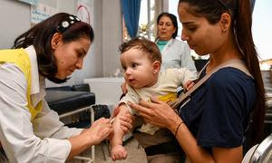 Восьмимесячному мальчику делают прививки от полиомиелита и кори в медицинском центре на юге Сирии.