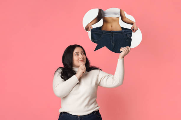 Overweight girl dreaming about slim fit body Weight Loss Concept. Overweight woman dreaming about slim fit body, holding and looking at her dream sporty figure in speech bubble, pink background slim fit healthy ladies stock pictures, royalty-free photos & images