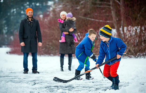 A father and mother watching their two sons play outdoor ice hockey.