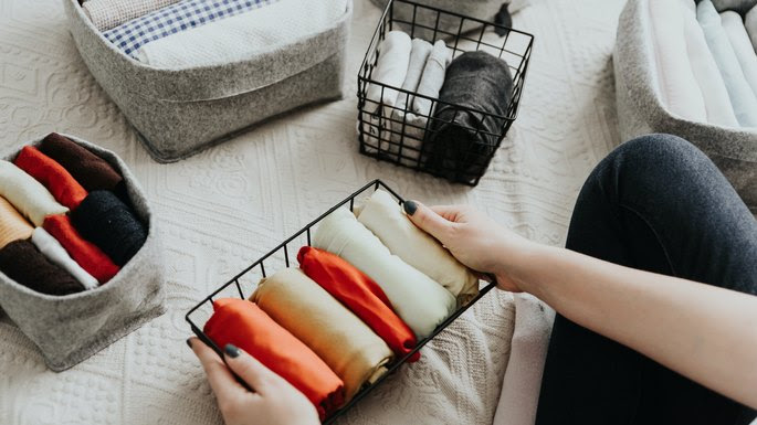 Folding clothes and organizing stuff in boxes and baskets. Concept of tidiness, minimalist lifestyle and japanese t-shirt folding system.