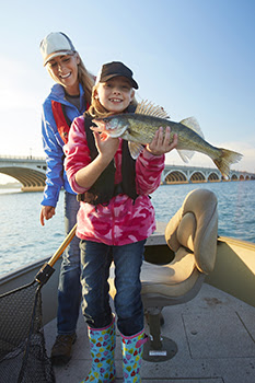 Smiling girl holding walleye and her mom in boat