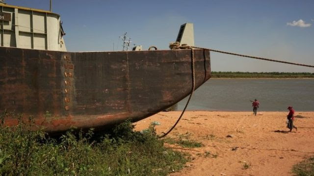 Pessoas passam por uma barcaça encalhada na margem do Rio Paraguai, afluente do Paraná, pois a falta de chuvas no Brasil, onde o rio nasce, baixou o nível das águas, obrigando os navios de carga a reduzirem a quantidade de grãos que são carregados para exportação, em Ypane, Paraguai 30 de agosto de 2021