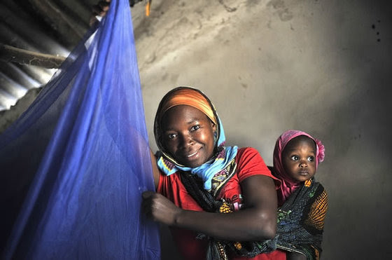 Mwajuma Ally Mandingo, 27, with her daughter Saidat, 9 months old, hangs a bed net in her house in Mtwara, Tanzania.