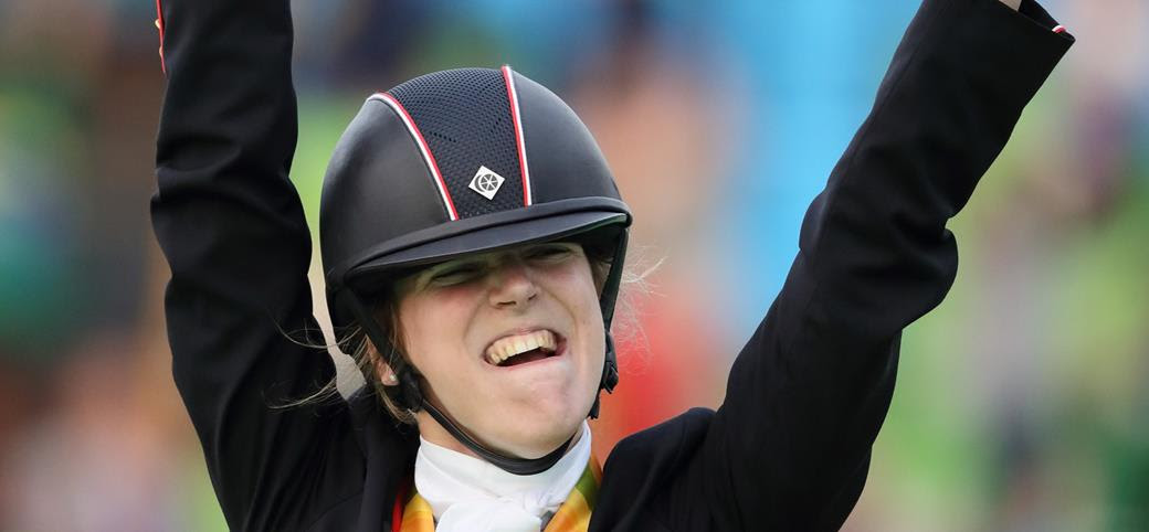 Sophie Christiansen, wearing her equestrian hat, cheering with her arms raised