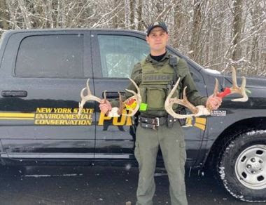 ECO holding two deer antlers while standing next to vehicle