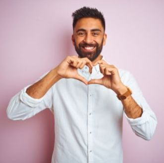 Young indian businessman wearing elegant shirt standing over isolated pink background smiling in love doing heart symbol shape with hands. Romantic concept.