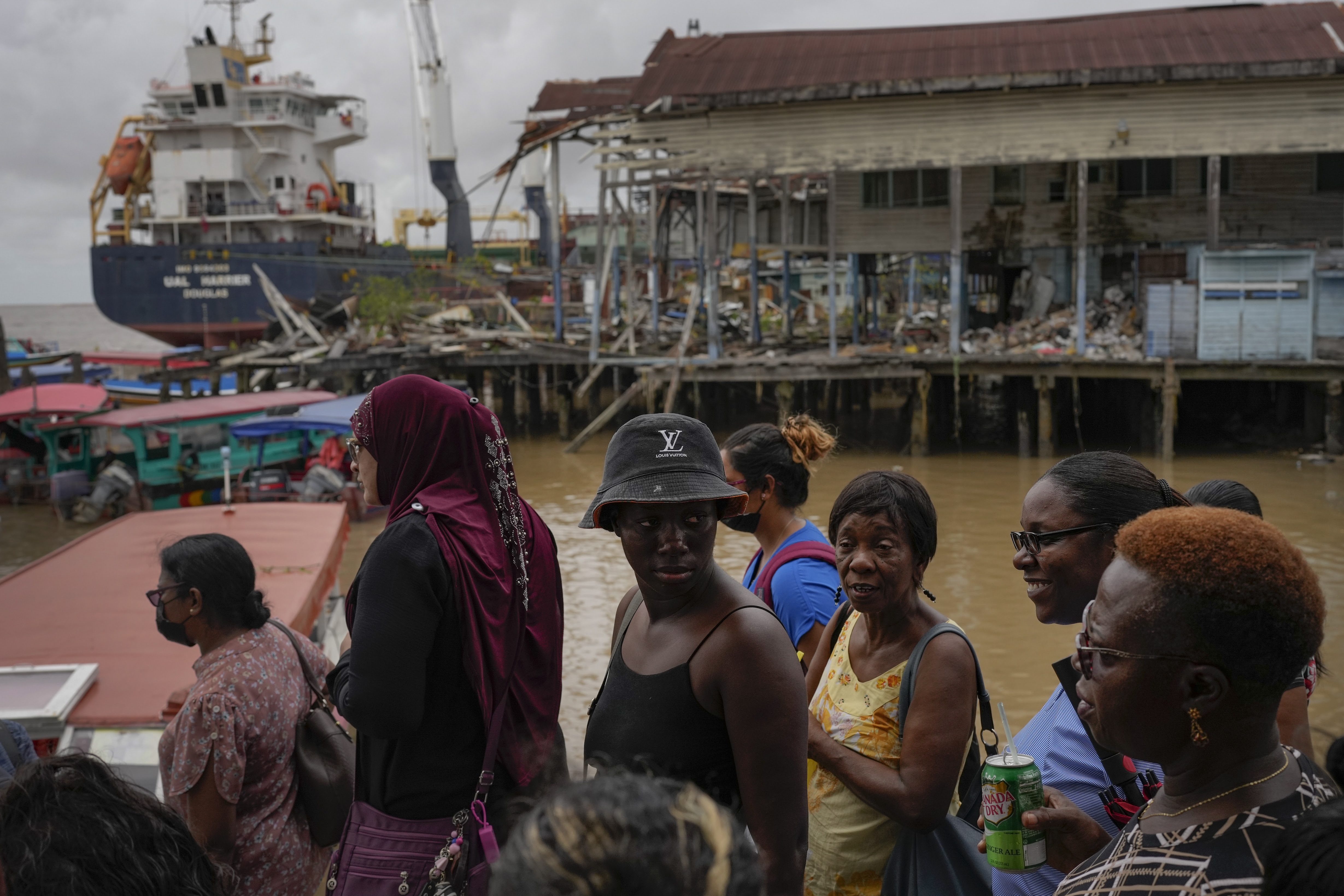 People wait at the Stabroek Market to ferry across the Demerara River, near a container ship in Georgetown, Guyana