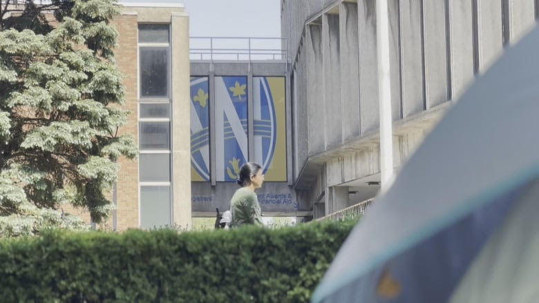 A student walks by a University of Windsor logo. The edge of a tent is in the foreground of the picture.