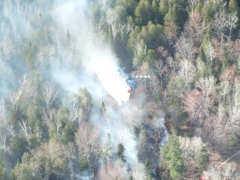 A Michigan State Police helicopter equipped with a Bambi Bucket carries a load of water over the forest.  