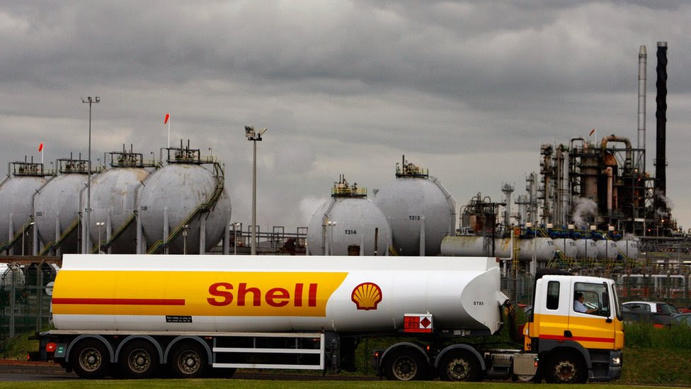 A Shell oil truck passes in front of an oil refinery