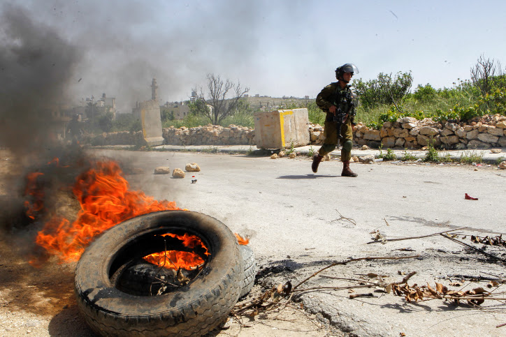 A soldier walks past a burning tire near Hebron. Archive: April 16, 2016
