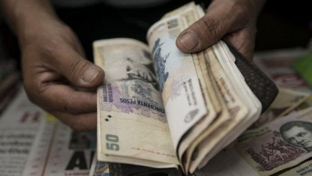 Close nas mãos de uma pessoa manuseando notas de peso argentino