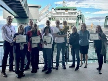 Several people posing for a photo at a ferry terminal with some holding up awards and certificates