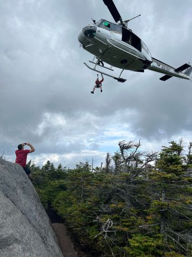 Helcopter hovers as Forest Rangers dangles from a rope during a rescue