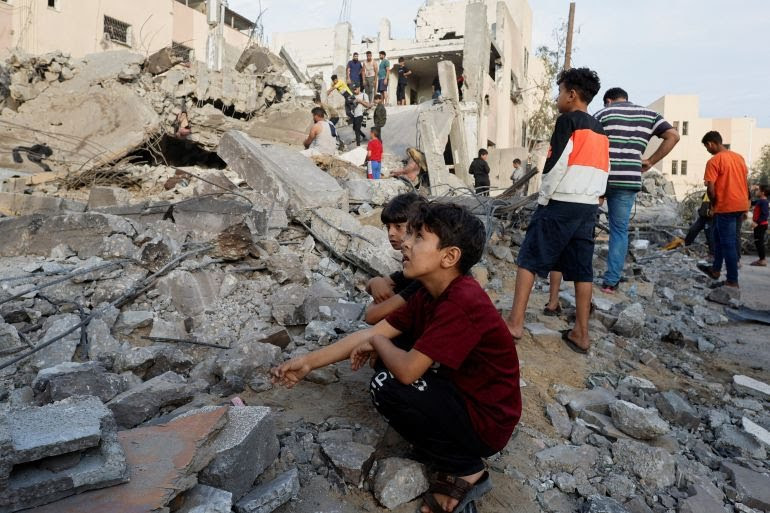 Palestinian children sit amid the rubble as others inspect a building destroyed in Israeli raids in Khan Younis in the southern Gaza Strip