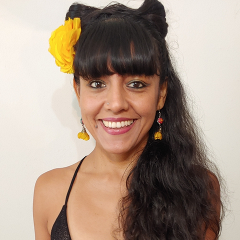 Silvita is wearing a black shiny dress, with a yellow flower on her right side of her long wavy black hair in a white background.