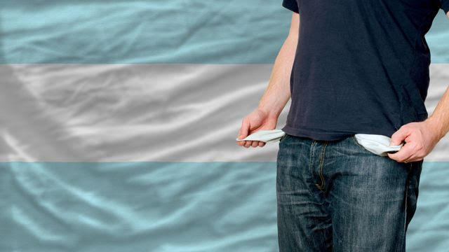 Um homem mostra seus bolsos vazios na frente de uma bandeira da Argentina