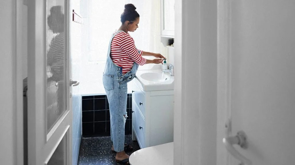 a pregnant woman washes her hands at the bathroom sink