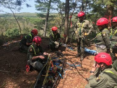 Rangers prepare for rope training in the woods at the edge of a cliff
