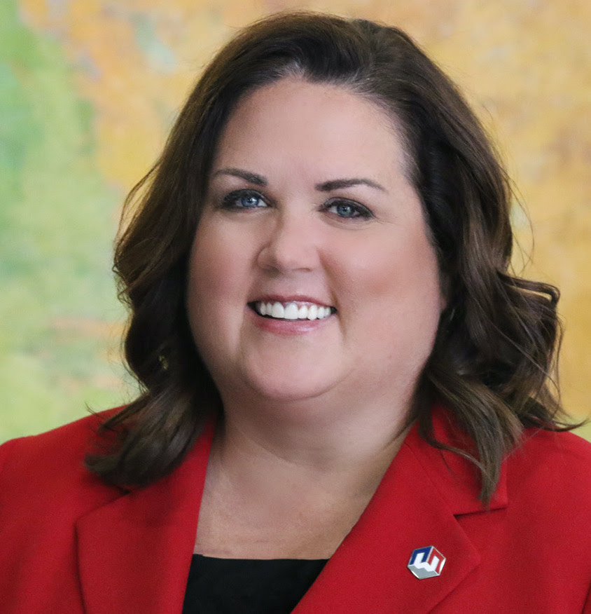 A photo of Casey Cameron dressed professionally. She is smiling and wearing a red blazer with a black shirt underneath and has a Workforce Services pin on her lapel.