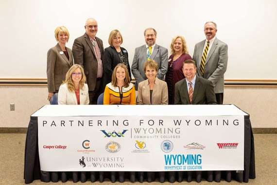 University of Wyoming President Laurie Nichols sits with WDE Chief Academic Officer Shelley Hamel, Wyoming Community College Commission Executive Director Sandra Caldwell, and the presidents of all seven of Wyoming's community colleges at a ceremonial signing of the Memorandum of Understanding. A Banner includes everyone's logo and reads, "Partnering for Wyoming."