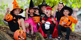 A group of small children dressed as witches and devils making scary faces and waving.