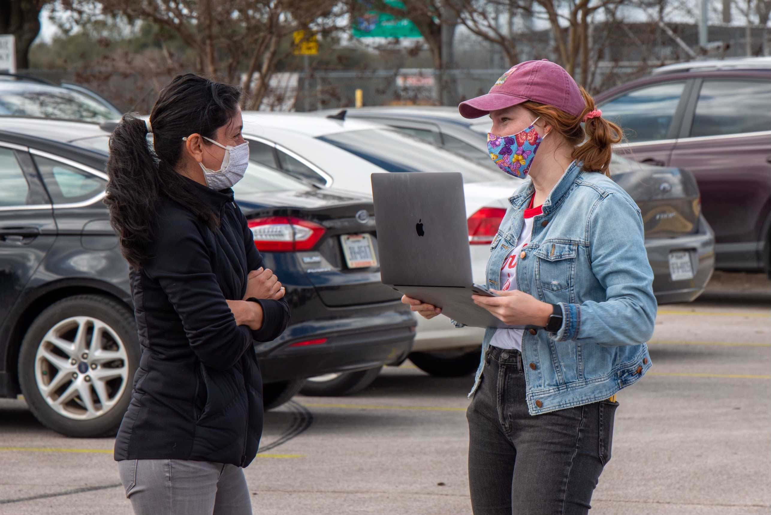 Powered by People volunteer wearing a mask with a clipboard, signing in volunteers to distribute water in Austin, Texas