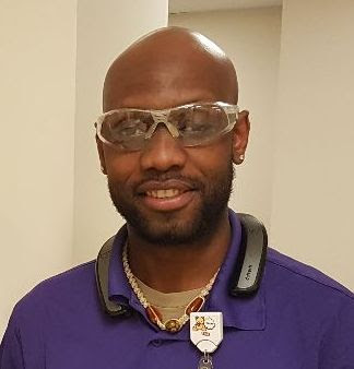 Jean in his purple uniform and safety glasses at his workplace