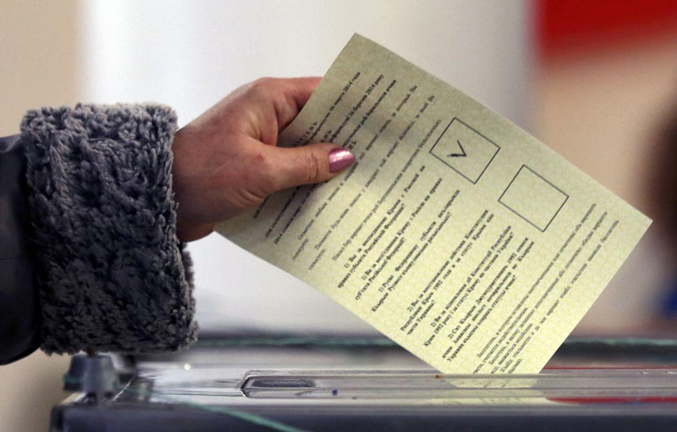 Una mujer introduce su voto en una urna electoral.