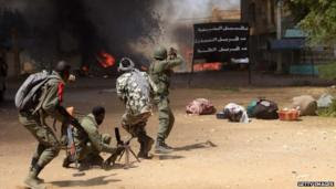 Malian troops point their guns towards smoke and flames caused by a car bomb