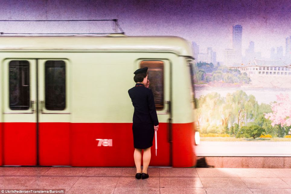 On the move: A female train guard waits for a train on North Korea's metro system in front of a mural painted on the far wall
