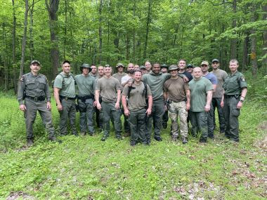Rangers pose for group picture with people taking the land navigation course in the woods